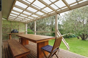 Eine Terrasses mit Holztisch und -stühlen, einem Grill und Blick ins Grün.