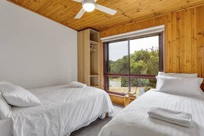 Ein Zimmer mit zwei Betten, Holzboden und einem großen Fenster mit Blick auf Bäume.
