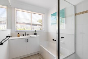 Un bagno moderno con una vasca, una cabina doccia in vetro e una finestra con persiane.