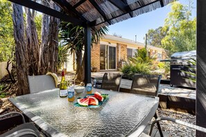 Un'area pranzo all'aperto con tavolo, sedie, barbecue e una casa sullo sfondo.