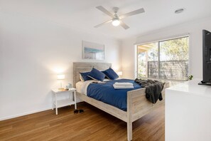Ein Schlafzimmer mit einem Bett, Nachttischen, einem Deckenventilator, einem Fenster mit Jalousien und einem Fernseher.