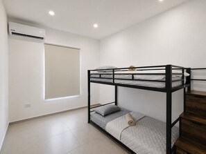 A bunk bed room with a window, white walls, and a ceiling air conditioner. - Brand NEW Calishi Apartment; Comfort & Style (Oranjestad)