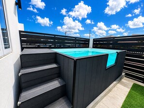 A modern outdoor swimming pool with a wooden deck and steps leading to it, surrounded by a fence. - Brand NEW Calishi Apartment; Comfort & Style (Oranjestad)