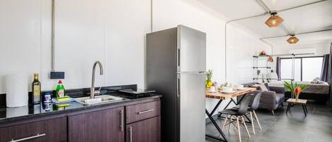 A modern kitchen with dark cabinetry, a stainless steel refrigerator, and a dining area with a table and chairs.