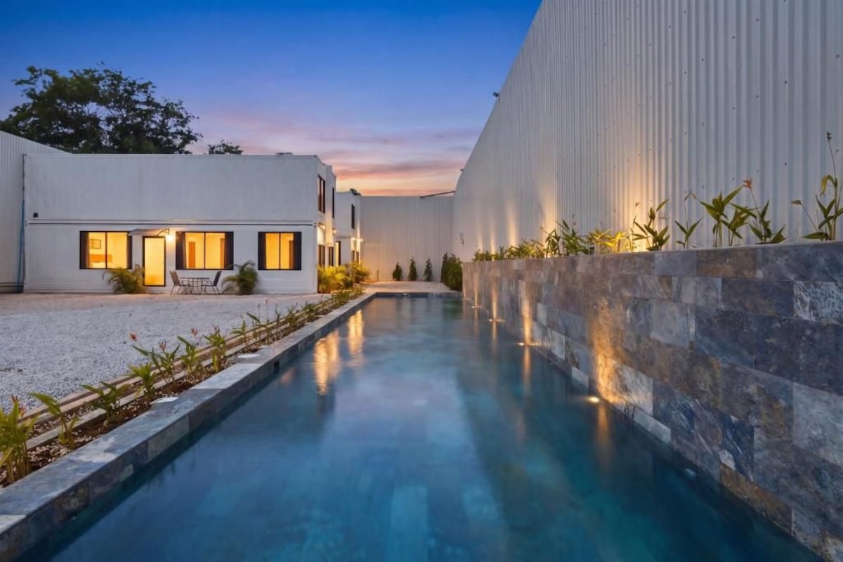 A modern building with a swimming pool, outdoor seating, and a well-lit entrance.
