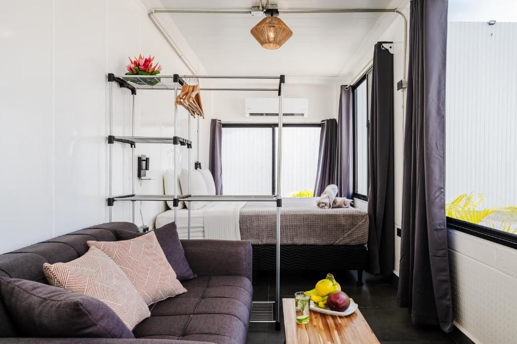 A modern interior with a sofa, a small table with fruits, a bed, and a window with curtains.