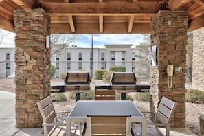 An outdoor patio with stone pillars, a table, and two barbecue grills.