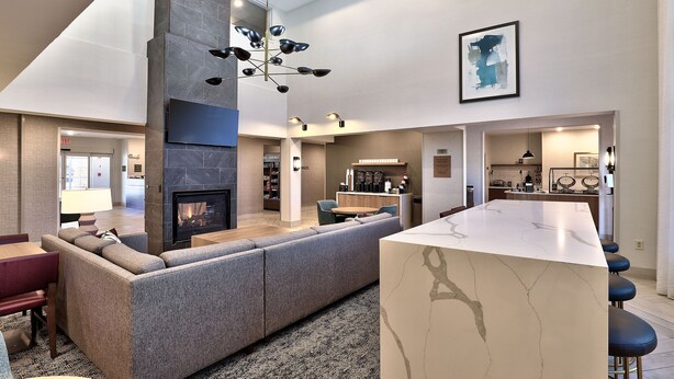 A modern living room with a fireplace, a large sofa, a dining area, and a kitchen in the background. - 2BR Accessible Suite | Free Hot Breakfast + Pool (Albuquerque)