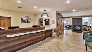 A hotel reception area with a wooden reception desk, a painting on the wall, and a herringbone patterned floor. - 2BR Accessible Suite | Free Hot Breakfast + Pool (Albuquerque)