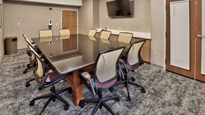 A conference room with a glass table surrounded by chairs, a mounted TV, and a door with blinds. - 2BR Accessible Suite | Free Hot Breakfast + Pool (Albuquerque)