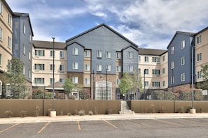A multi-story residential building with a central entrance, a parking lot in front, and a clear sky.