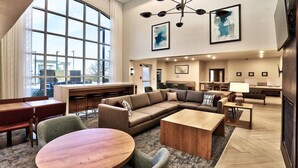 Eine großzügige Lobby mit einem großen Fenster, einem Ecksofa, einem runden Tisch und einer modernen Deckenleuchte.