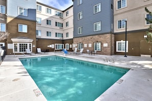 A swimming pool with lounge chairs, a covered area, and a building with multiple windows and a door.