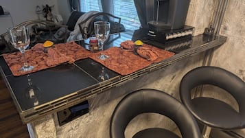 A kitchen counter with a coffee maker, two glasses, a wine glass, and a decorative plate.