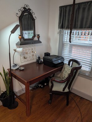 A wooden desk with a lamp, a printer, and a chair with a cushion.