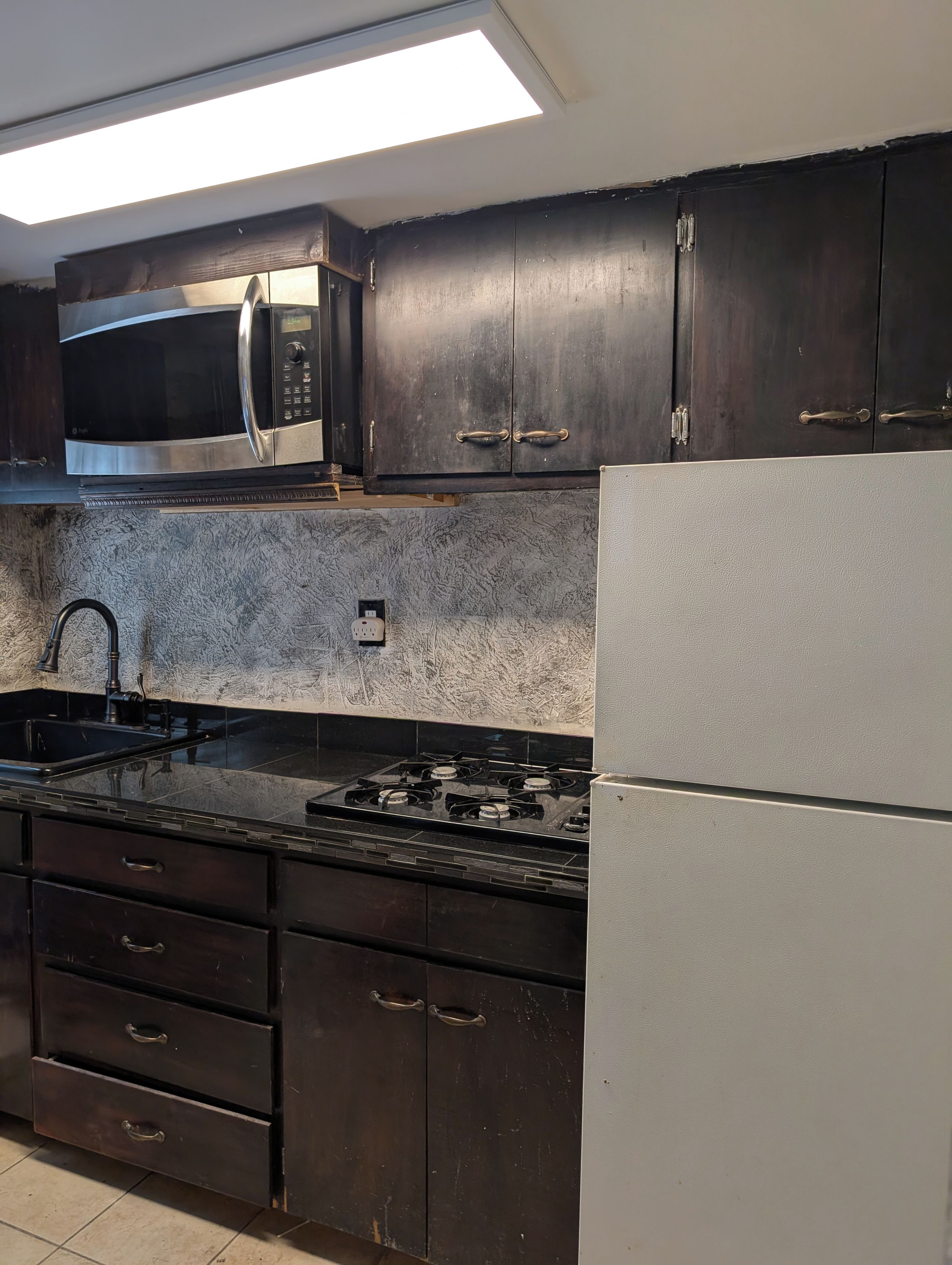 A kitchen with dark cabinets, a stainless steel microwave, a gas stove, and a white refrigerator.