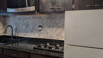 A kitchen with dark cabinets, a stainless steel microwave, a gas stove, and a white refrigerator.