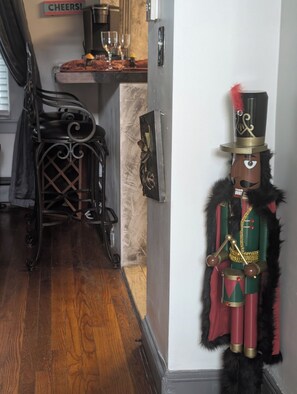 A nutcracker figurine mounted on a wall, a kitchen area with a sign that says 'CHEERS!', and a staircase with a banister.