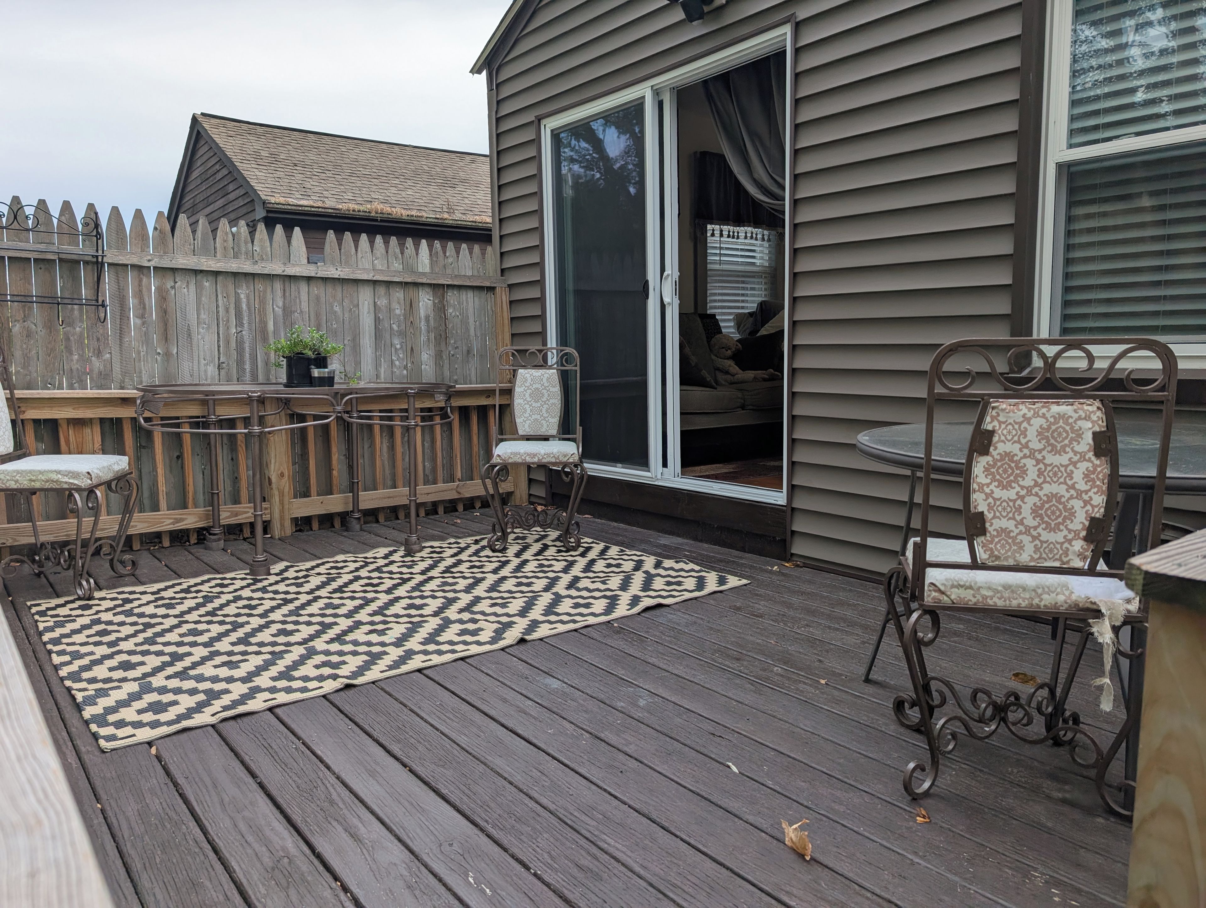 A deck with a patterned rug, metal chairs, and a table.