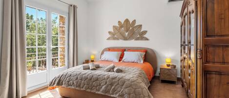 Un dormitorio con cama, mesita de noche, armario de madera y una ventana grande con cortinas.
