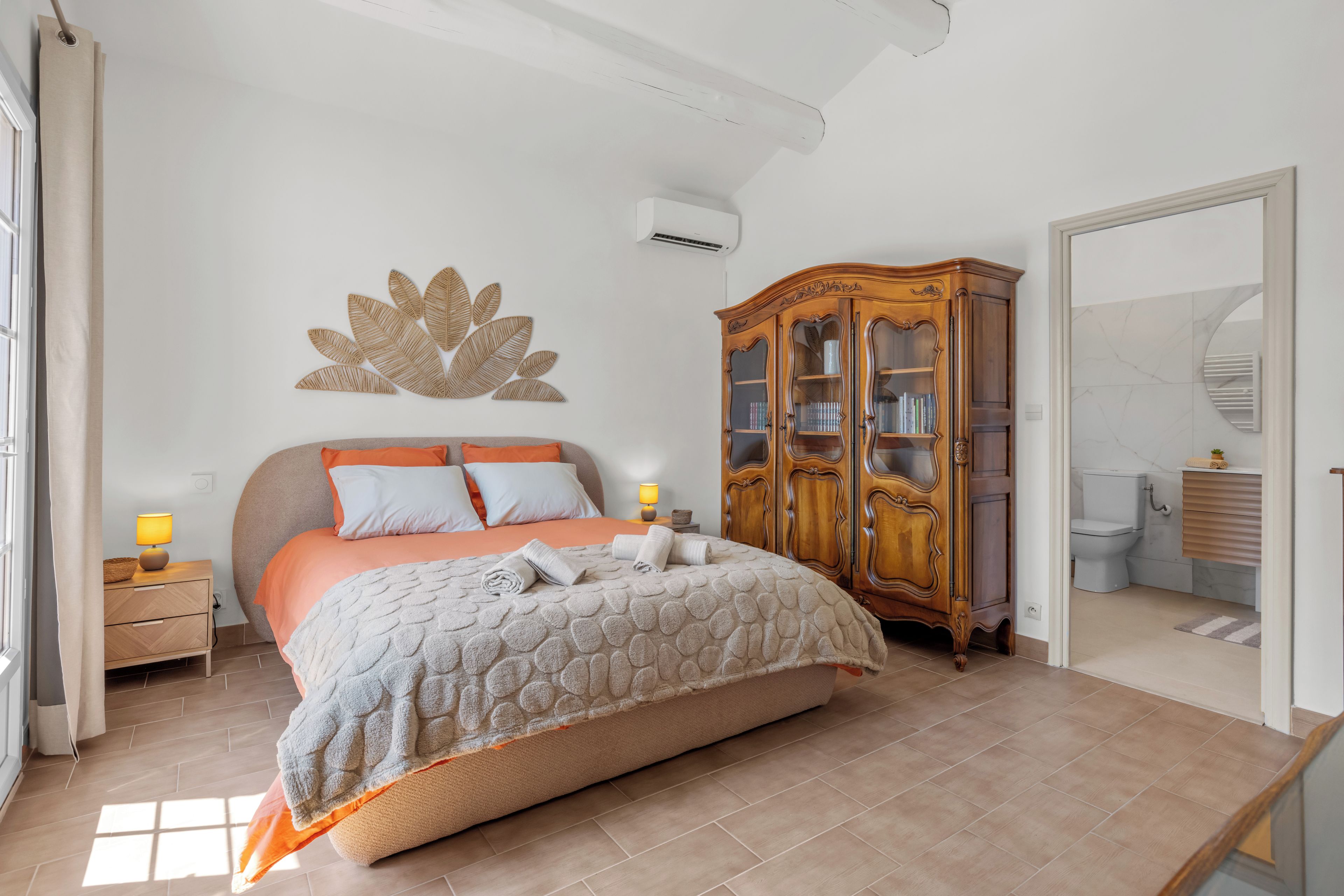 Quarto com cama, armário de madeira, banheiro e uma janela grande.