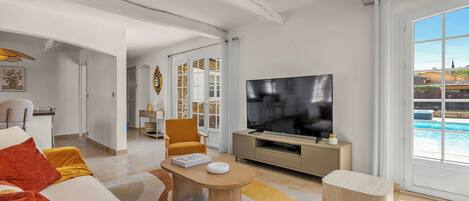 Sala de estar ampla com TV grande, sofá, mesa de centro e vista para uma piscina.