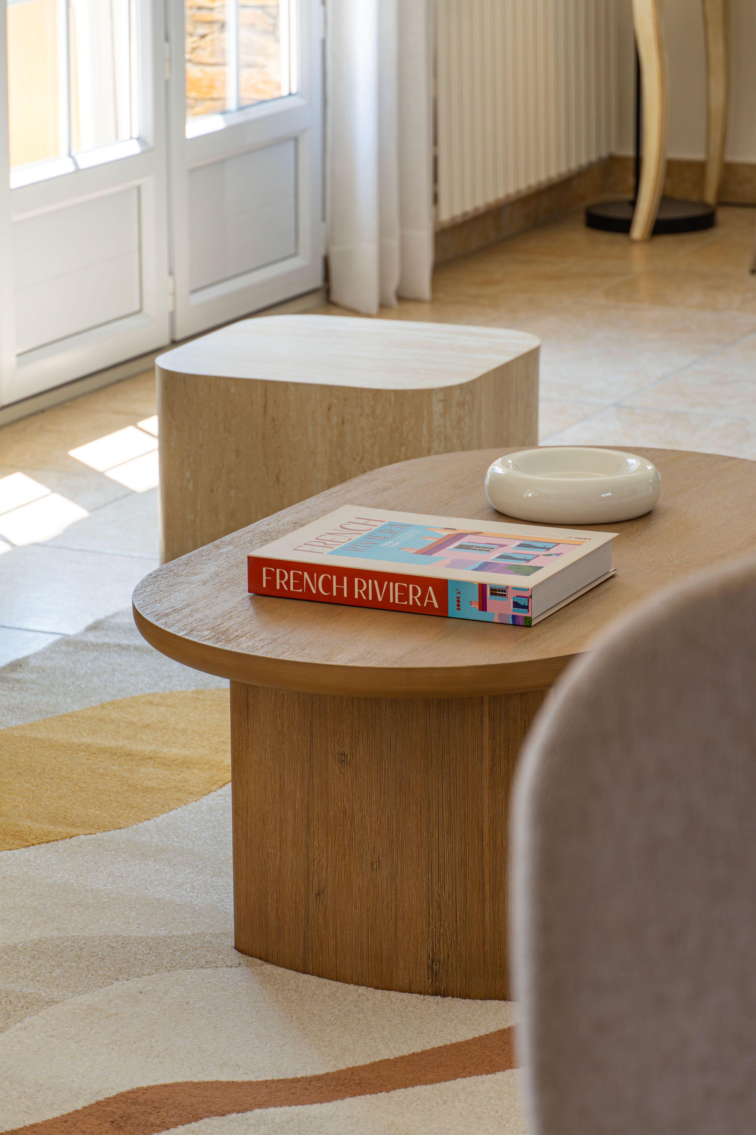 Una mesa de madera redonda con un libro titulado 'FRENCH RIVIERA' y un cuenco blanco encima.