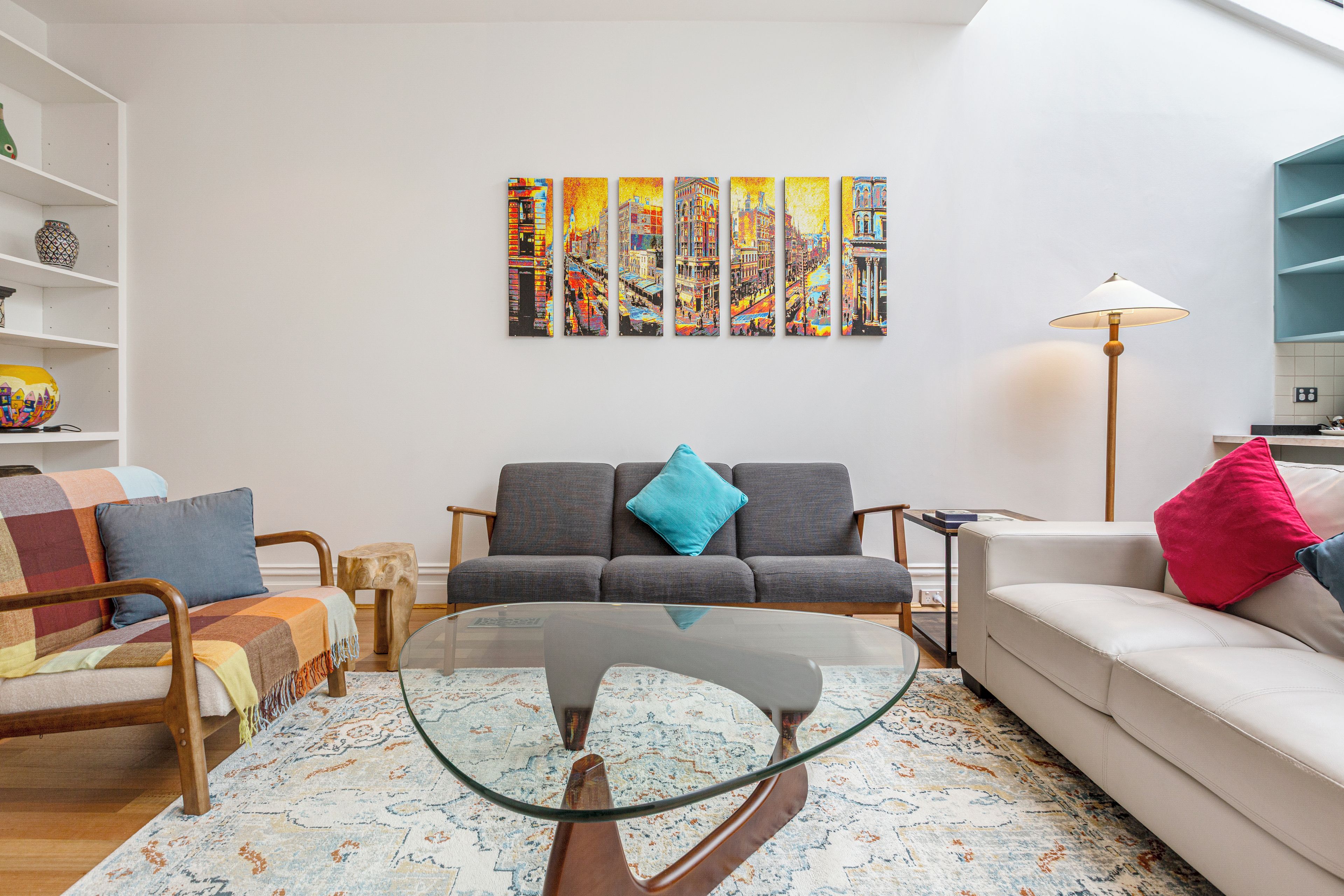 A living room with a sofa, armchair, coffee table, and a wall with colorful artwork.