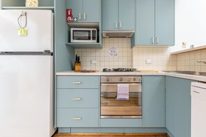 A kitchen with light blue cabinets, a white refrigerator, a microwave, a gas stove, and a stainless steel oven. - Skylight Terrace Timeless Stay near Parks and Cafs (Fitzroy North)