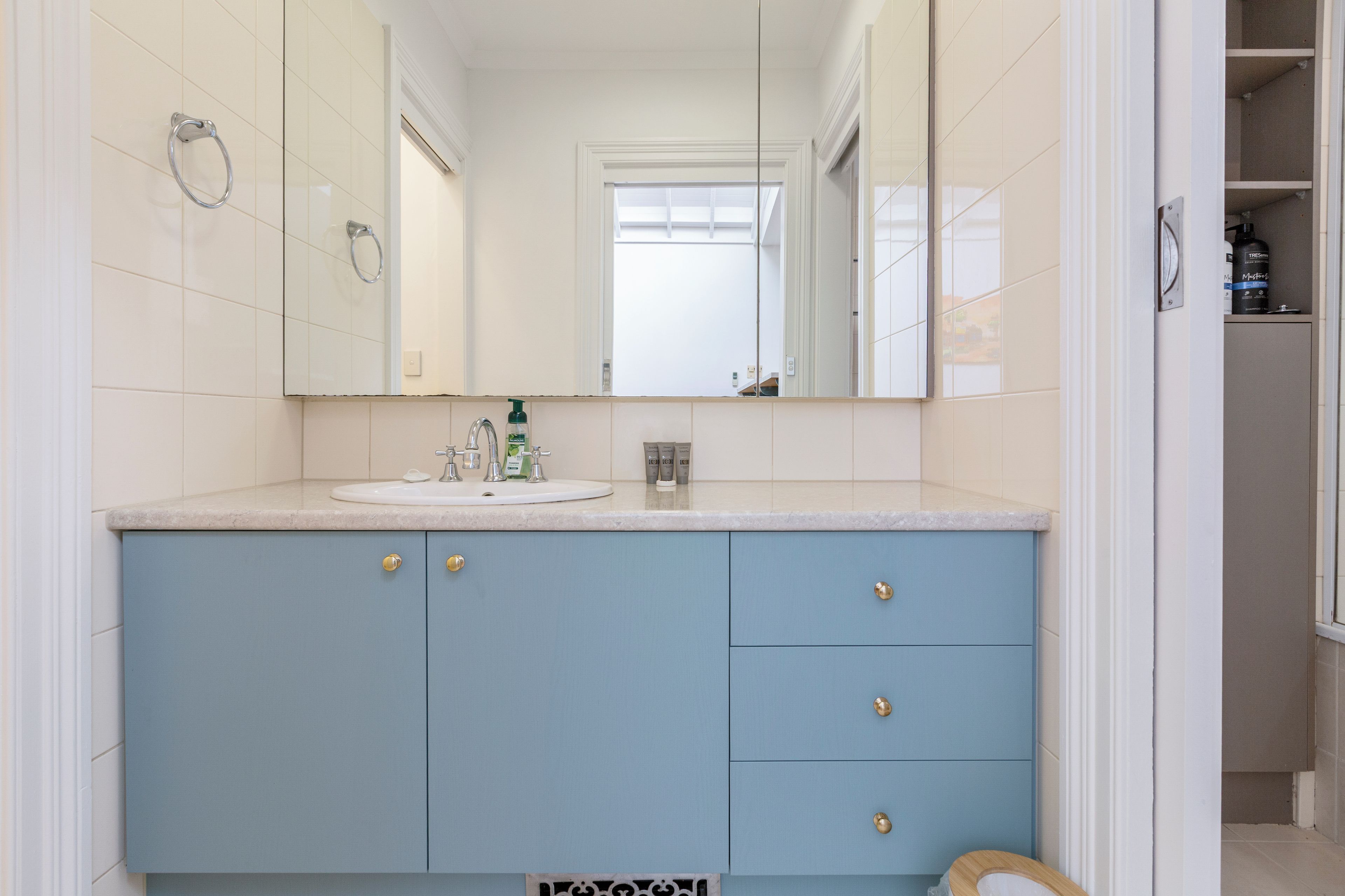 A bathroom with a white sink, blue cabinets, and a mirror reflecting a door and window.