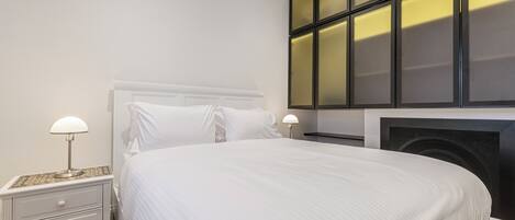 A neatly made bed with a headboard, two bedside lamps, and a nightstand with drawers.