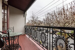 A balcony with a table and chairs, a view of a street with parked cars, and a tree with bare branches. - Skylight Terrace Timeless Stay near Parks and Cafs (Fitzroy North)