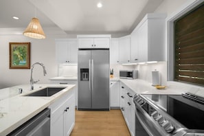 A modern kitchen with white cabinetry, stainless steel appliances, a marble countertop, and a pendant light. - Kiahuna Hale Kai II (Koloa)