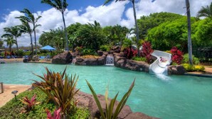 A pool with a water slide, surrounded by tropical vegetation and palm trees. - Kiahuna Hale Kai III (Koloa)