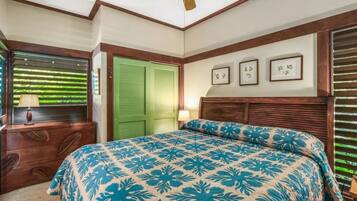 A bedroom with a bed, a nightstand, a lamp, a window with blinds, and a green door.