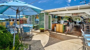 An outdoor dining area with tables and chairs, a bar area with a counter, and a green wall with a sign. - Kiahuna Hale Kai III (Koloa)