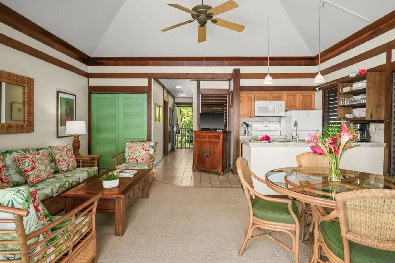 A spacious living area with a sofa, coffee table, and dining table with chairs. A kitchen with wooden cabinets and a microwave is visible in the background.
