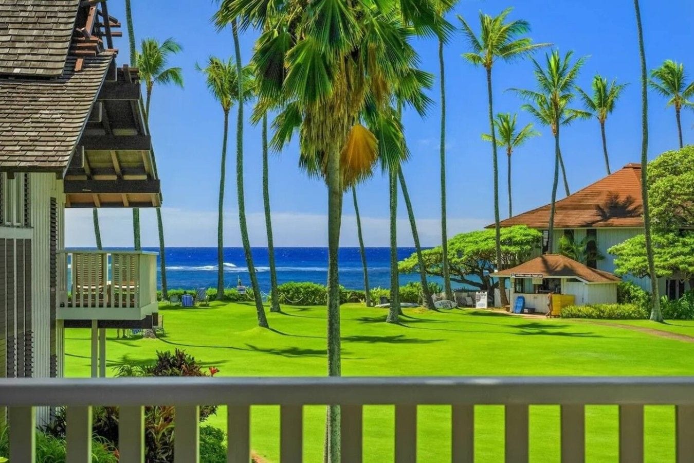 A beachfront property with a well-maintained lawn, palm trees, and a view of the ocean.