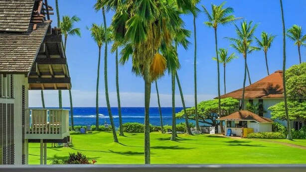 A beachfront property with a well-maintained lawn, palm trees, and a view of the ocean. - Kiahuna Hale Kai III (Koloa)