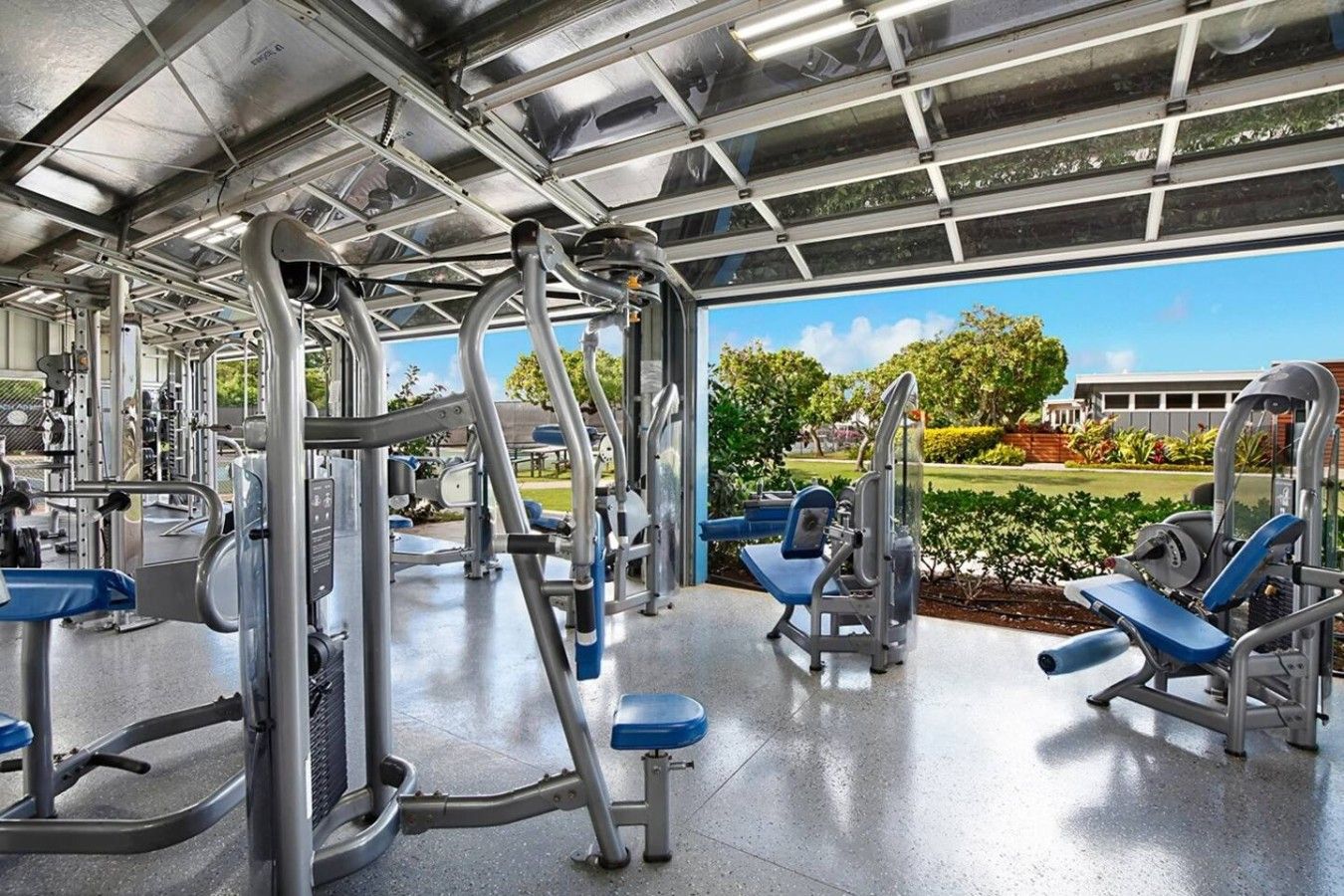 A gym with various exercise machines and a view of a green landscape.