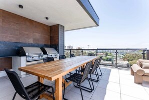 An outdoor patio with a wooden table and chairs, a grill, and a view of the city. - Top-Floor Hillcrest Penthouse w/ Balcony, Pool & Gym Near Zoo (San Diego)