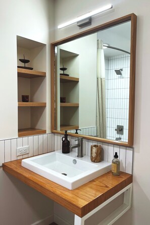 Un baño con lavamanos blanco, encimera de madera y un espejo grande.