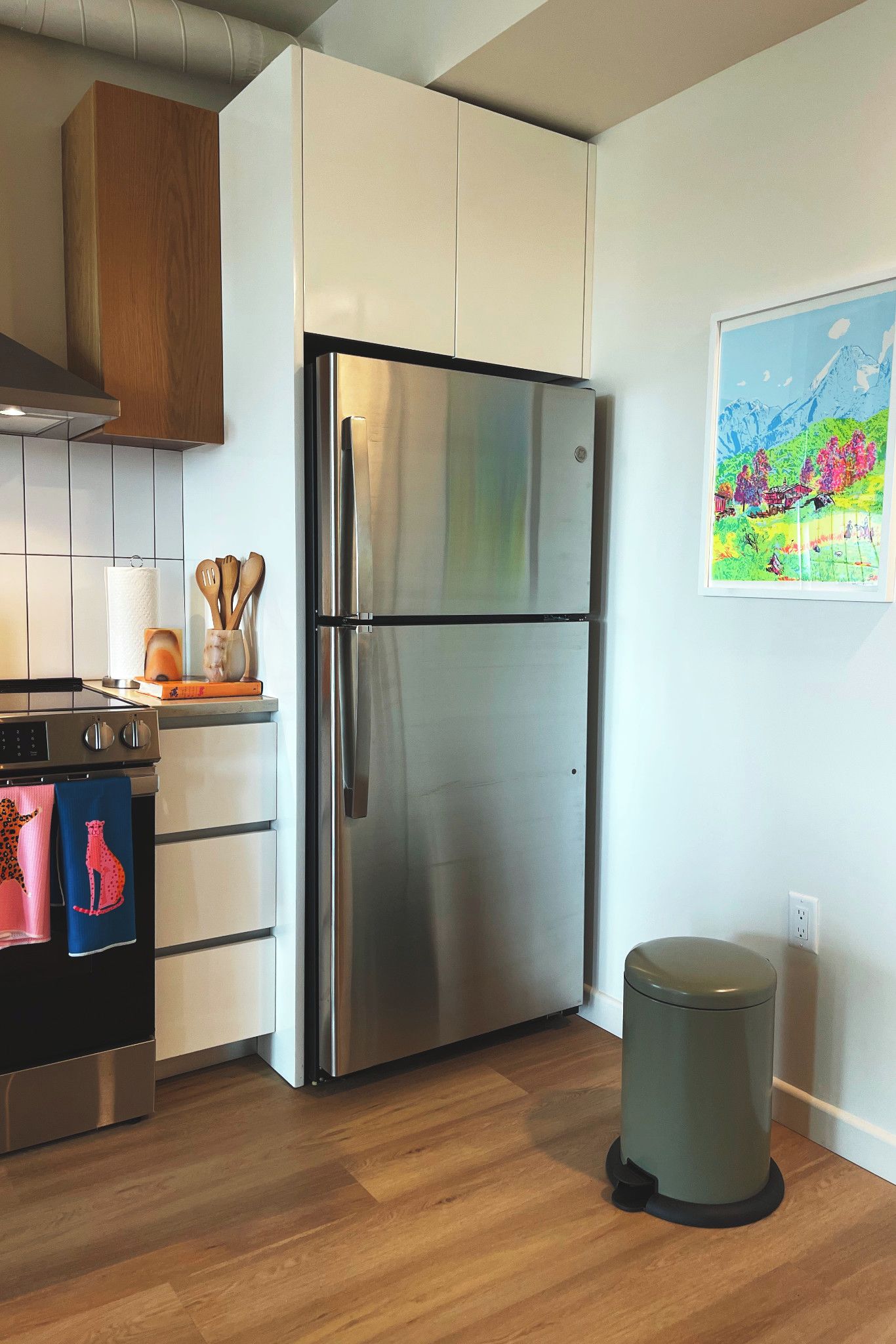 A modern kitchen with a stainless steel refrigerator, wooden cabinets, and a wooden floor.