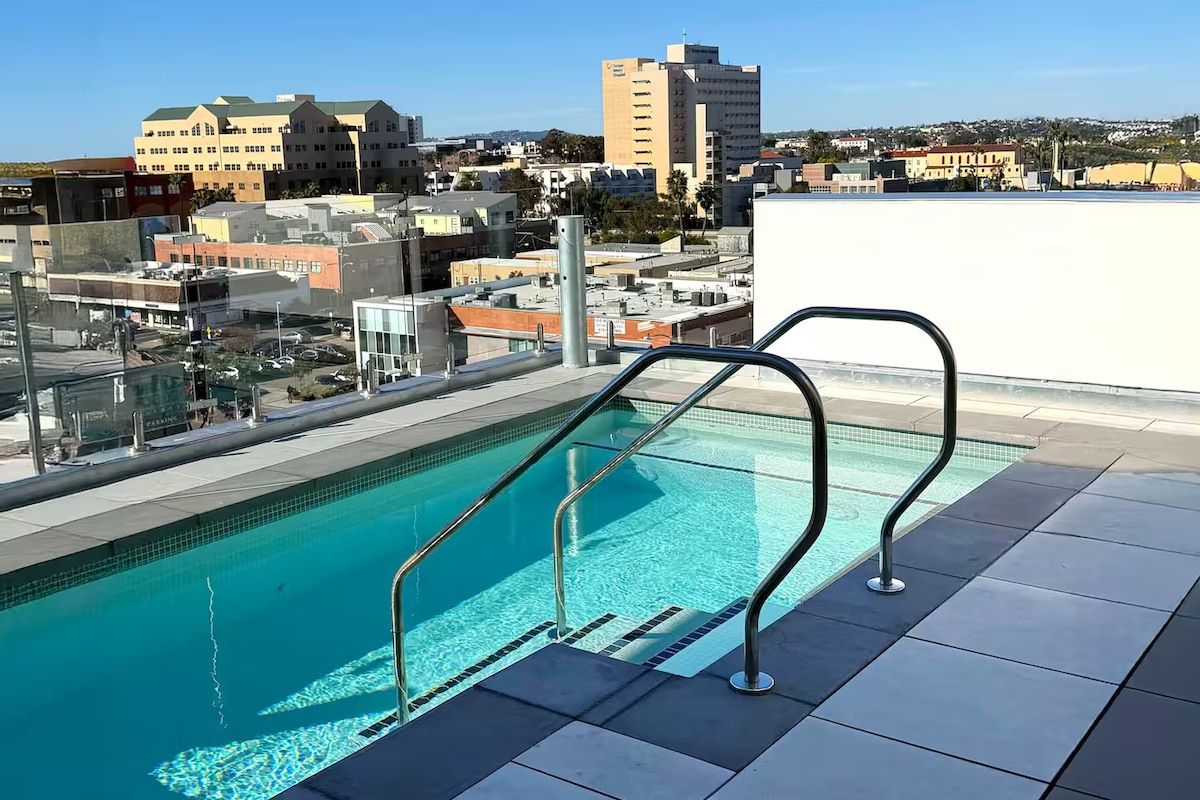 A rooftop swimming pool with metal railings, surrounded by city buildings.