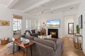 A living room with a fireplace, a sofa set, and a large window with blinds. - Spanish Hacienda w/ Breathtaking Mountain Views! (La Quinta)