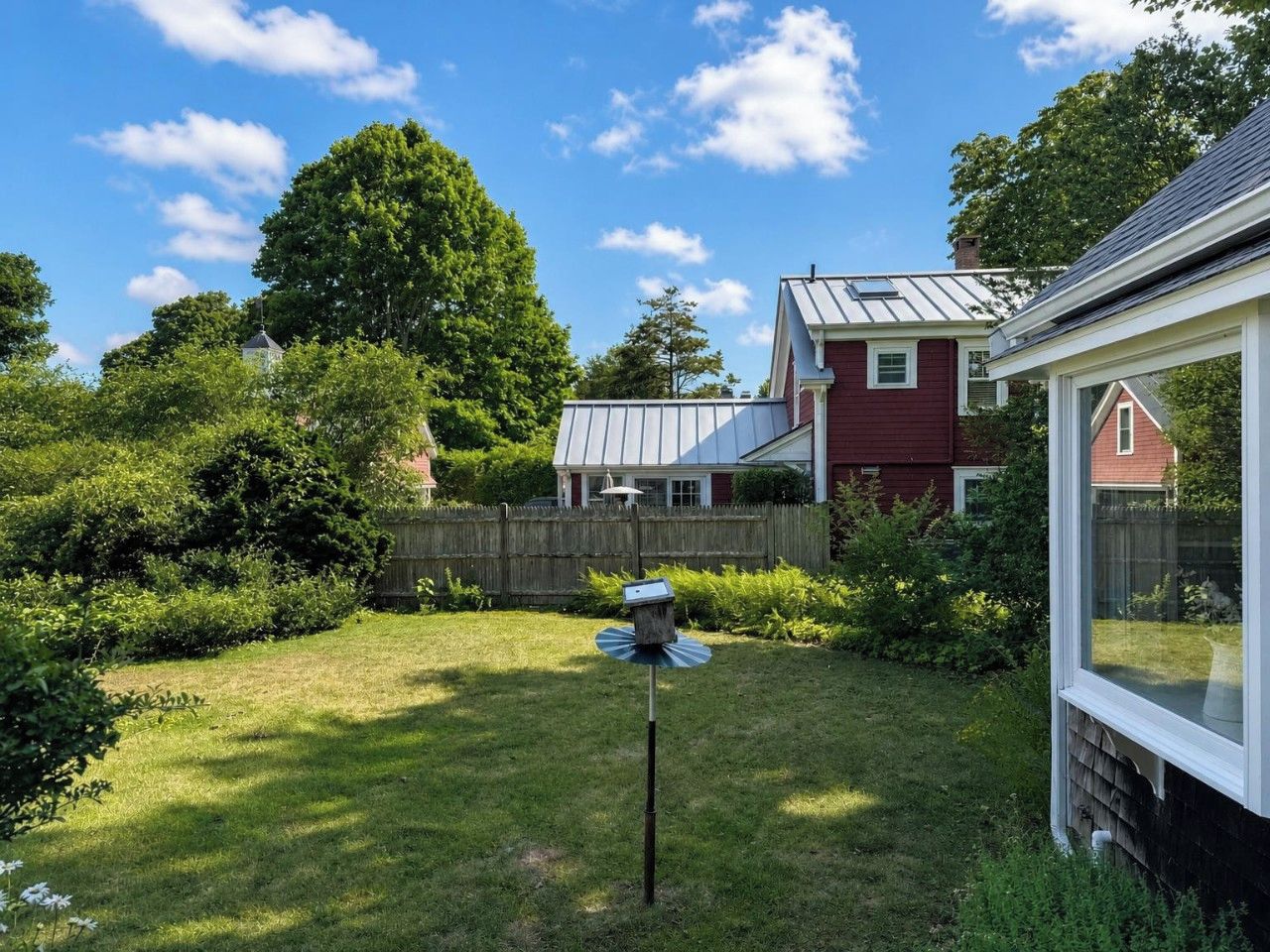A residential backyard with a bird feeder, a wooden fence, and a house with a red exterior and white trim.