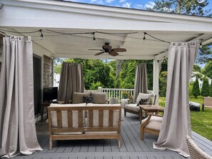 Een overdekt terras met een plafondventilator, comfortabele zithoeken en gordijnen.
