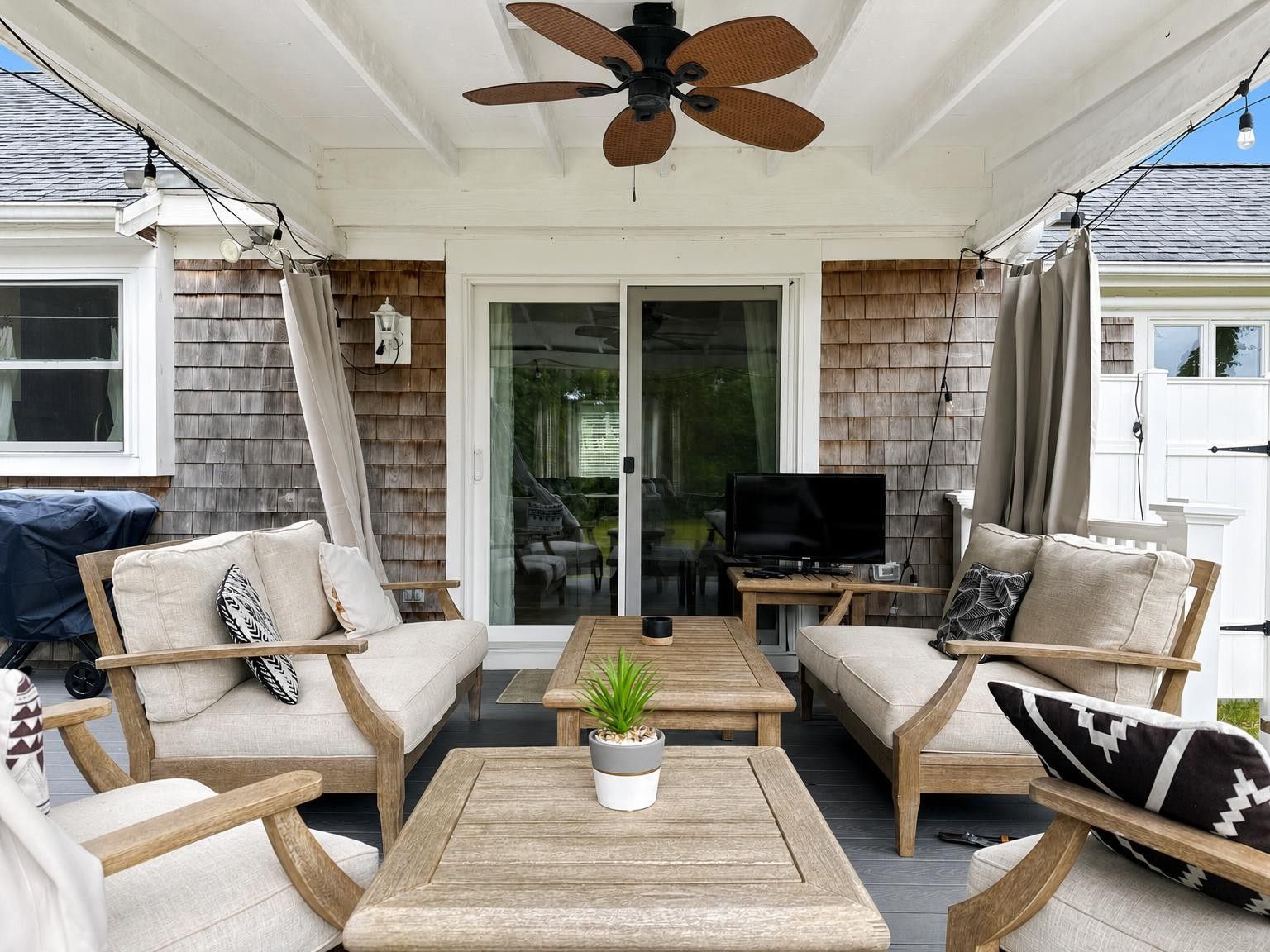 An outdoor patio with a ceiling fan, wooden furniture, and a television.