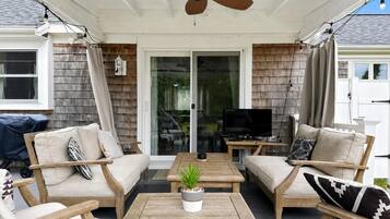 An outdoor patio with a ceiling fan, wooden furniture, and a television.