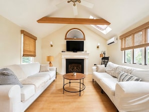 A spacious living room with a fireplace, two white sofas, a round coffee table, and a ceiling fan.
